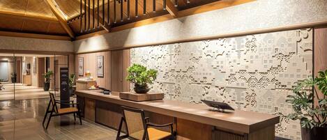 A reception area with a wooden reception desk, a potted plant, and a patterned wall.