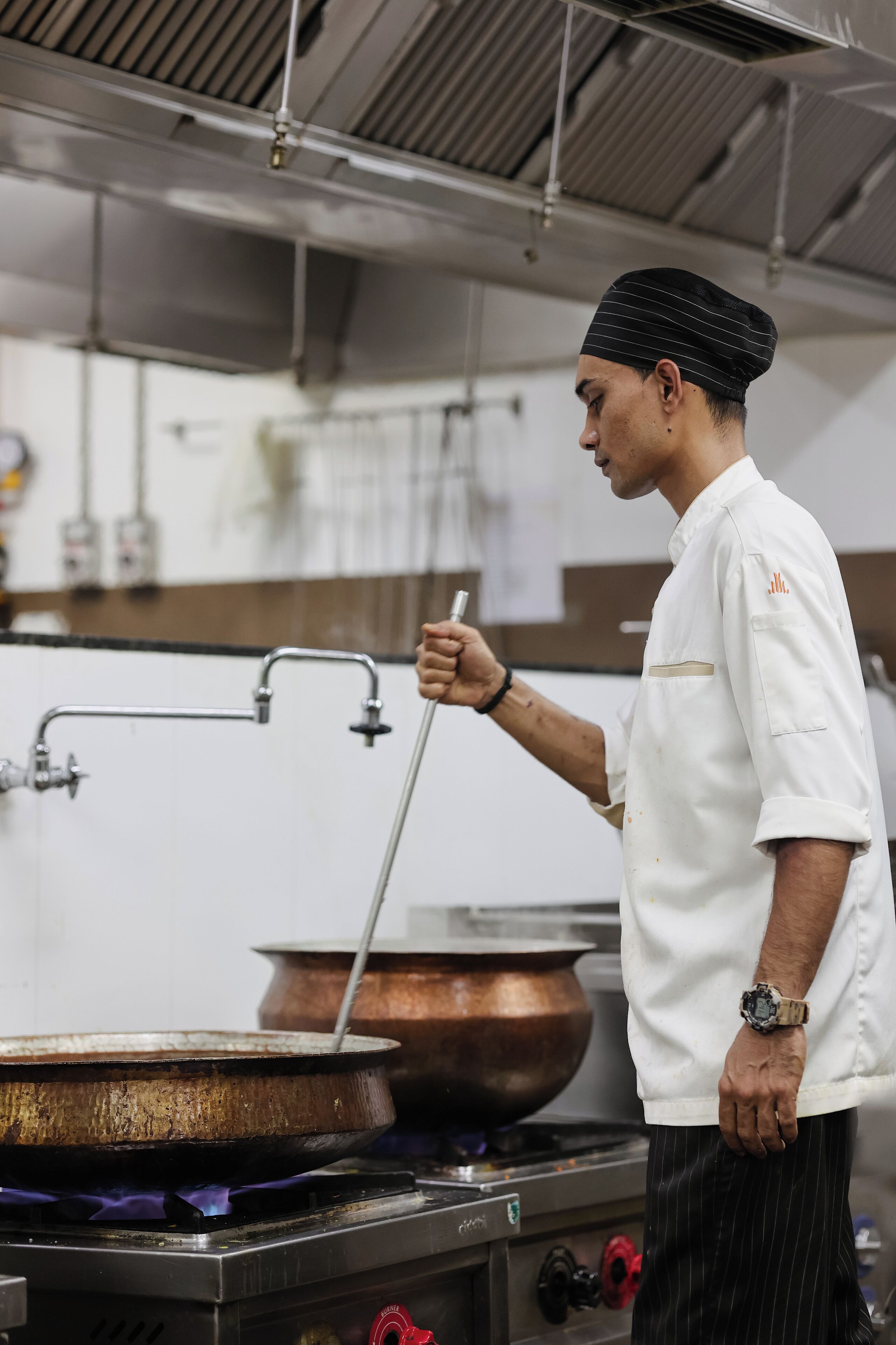 Un chef en una cocina profesional con equipo de acero inoxidable, una olla de cobre y una estufa a gas.