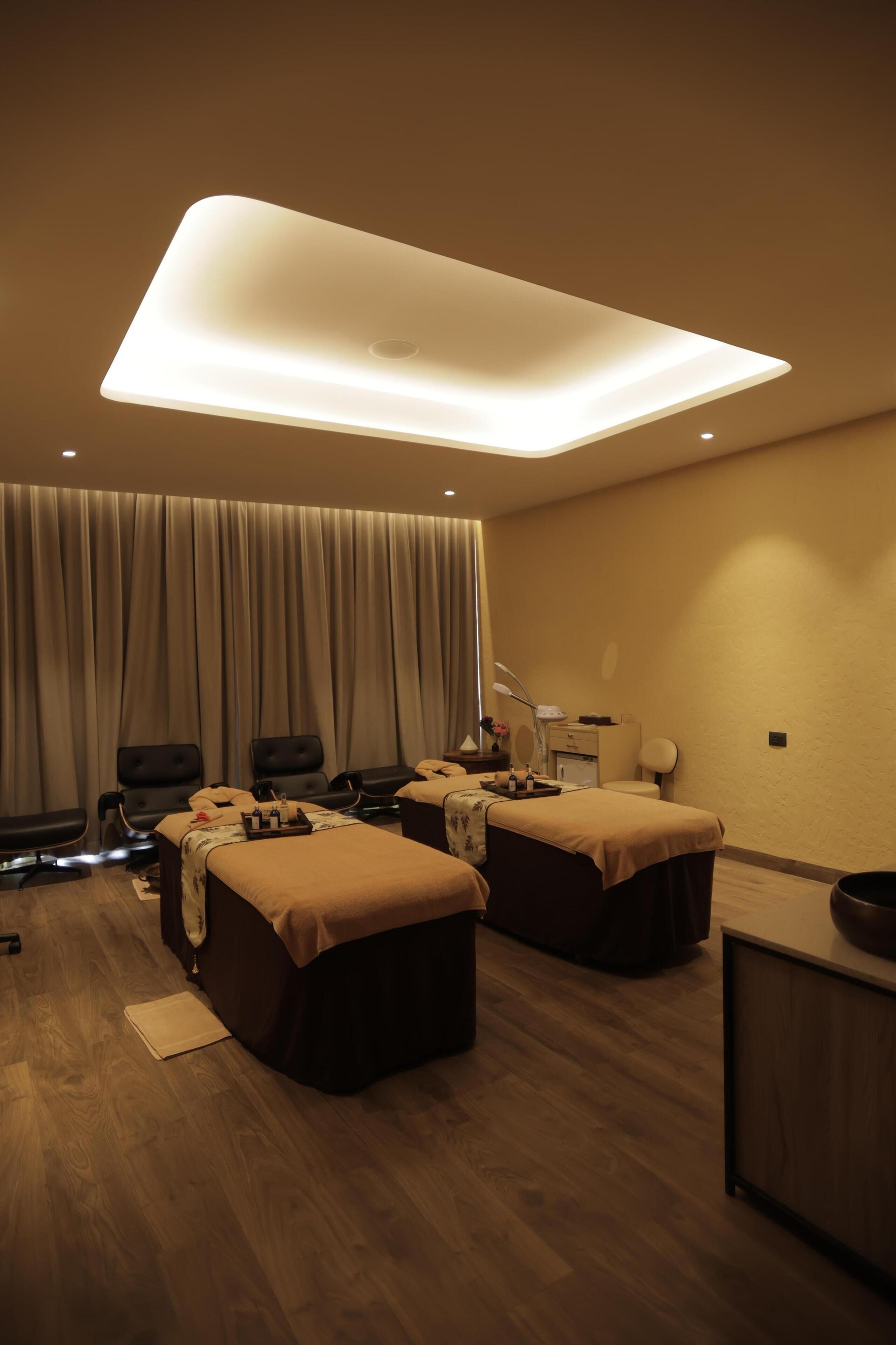 Un moderno cuarto de spa con dos camillas de masaje, una lámpara de techo grande y un telón de fondo.