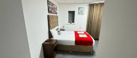 A hotel room with a bed, a nightstand, a window, and a small table.