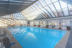 An indoor swimming pool with clear glass ceilings, lounge chairs, and a view of the outside. - Très bel appartement rénové avec piscine, tennis et parking privé 09 (Le Touquet-Paris-Plage)