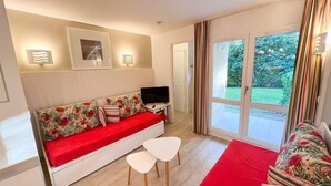 A modern living room with a sofa, a TV, and a small table. There is a sliding glass door leading to a garden.