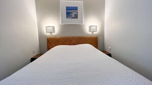 A neatly made bed with a white textured cover in a room with a simple, clean design.