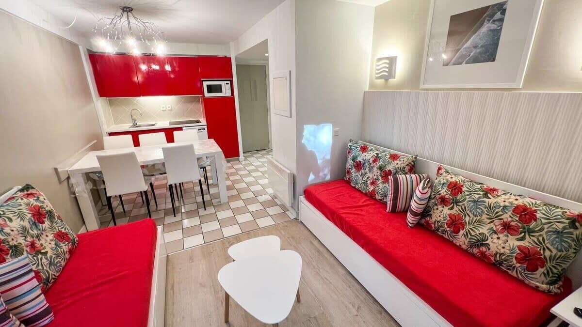 Un espace de vie compact comprenant un coin cuisine, un coin repas et un canapé agrémenté de coussins à motifs floraux.