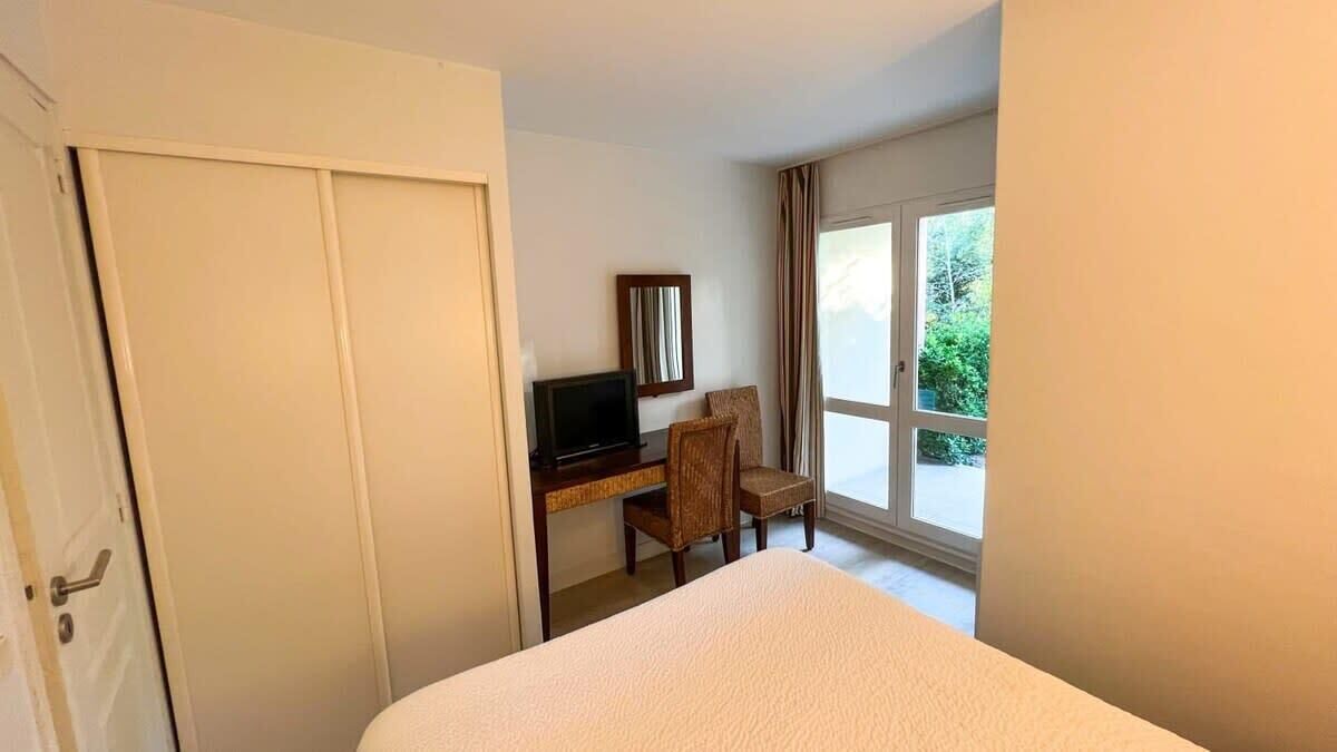 Habitación de hotel con cama, escritorio con computadora, una silla y ventana con vista a follaje.