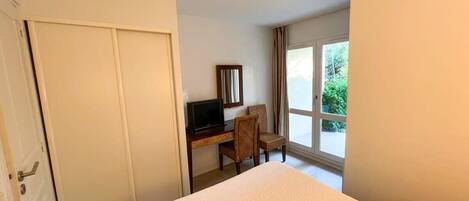 Habitación de hotel con cama, escritorio con computadora, una silla y ventana con vista a follaje.