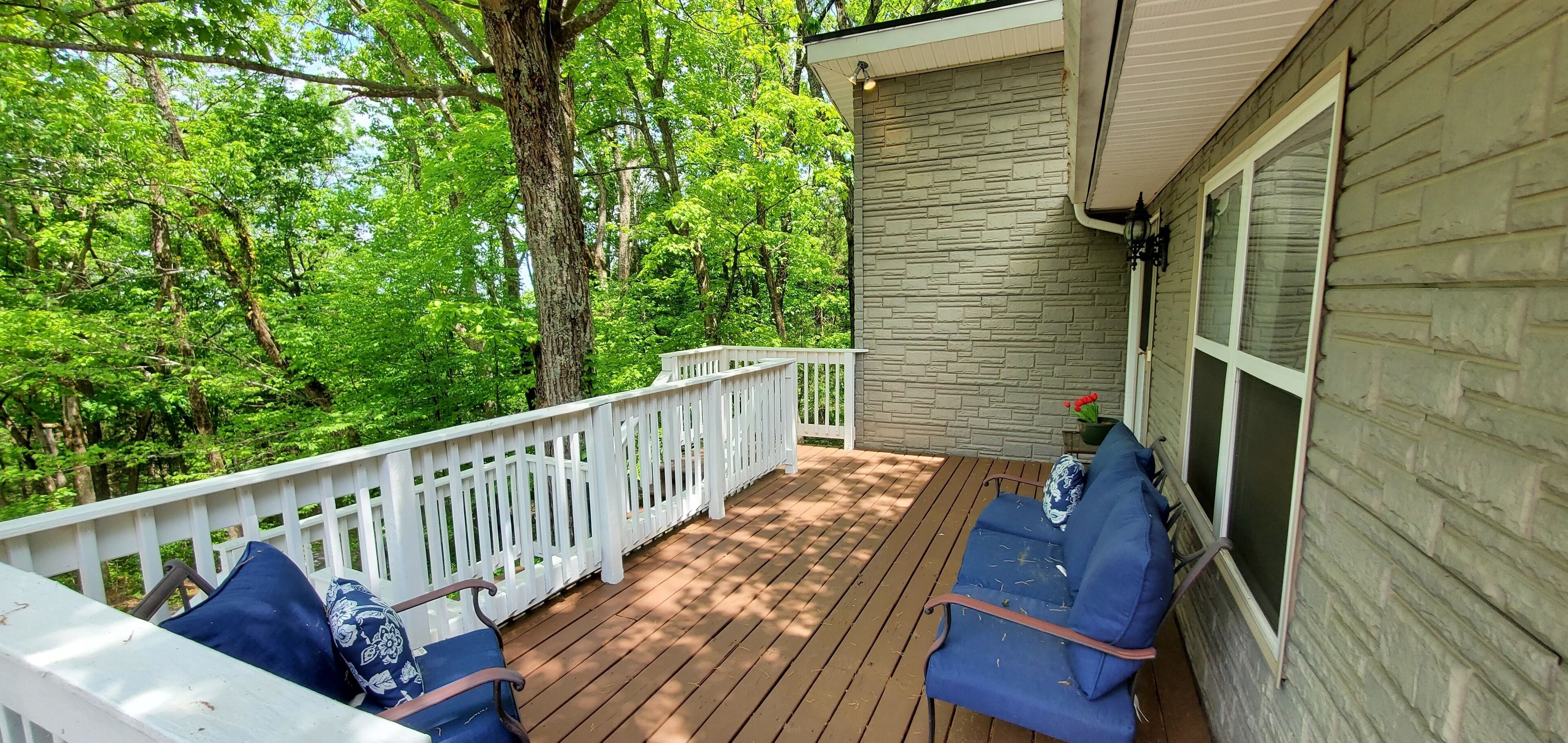 A wooden deck with two blue chairs and a white railing.