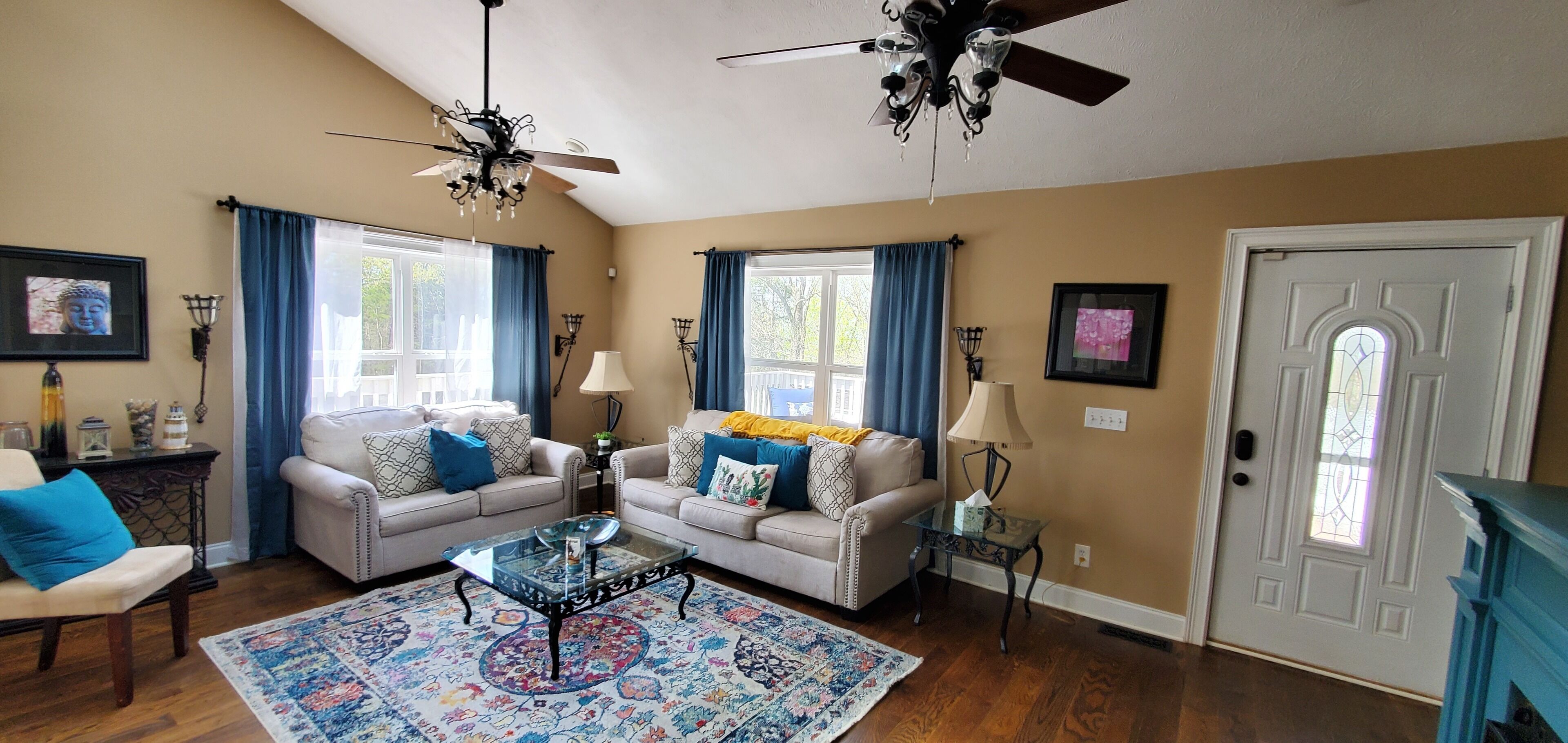 A living room with two sofas, a glass coffee table, a patterned rug, and a door with a stained glass window.