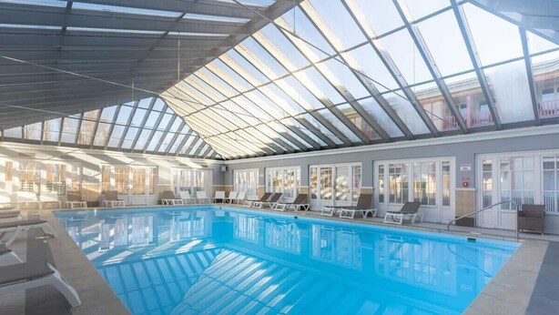 An indoor swimming pool with clear glass ceilings, lounge chairs, and a view of the outside. - Bel appt 6 p avec piscine, parking gratuit et tennis 109 (Le Touquet-Paris-Plage)