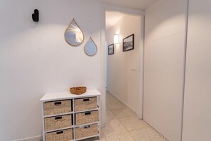Un couloir aux murs blancs, avec une console blanche agrémentée de paniers, ainsi que des miroirs et des cadres accrochés au mur.