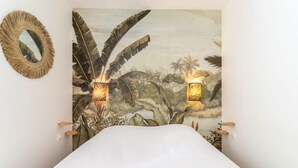 A bedroom with a large bed, a wall-mounted mirror, and two wall sconces with a tropical mural. - Bel appt 6 p avec piscine, parking gratuit et tennis 109 (Le Touquet-Paris-Plage)