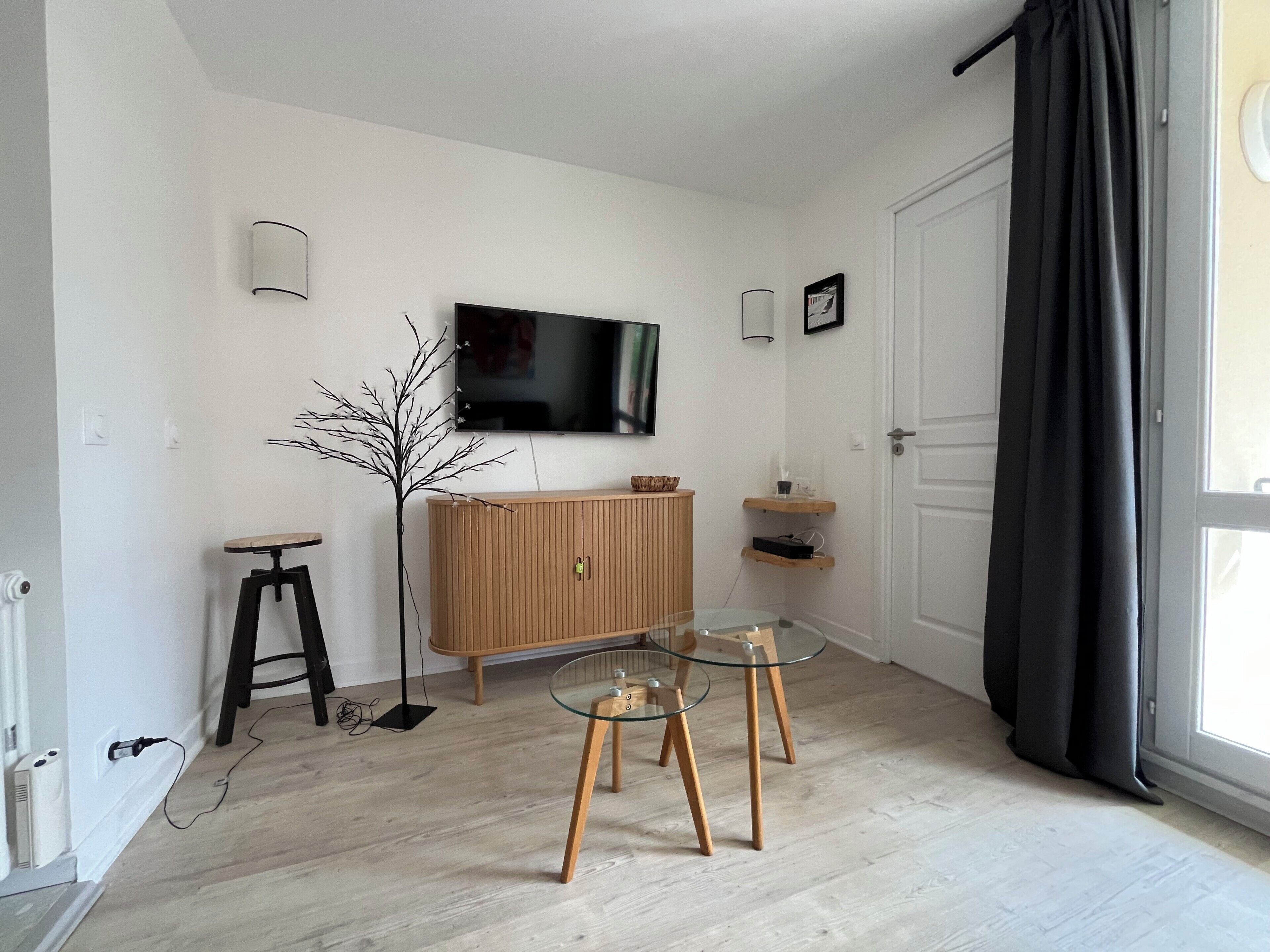 Un salon moderne avec un meuble en bois, une table en verre, un lampadaire noir et un téléviseur à écran plat fixé au mur.