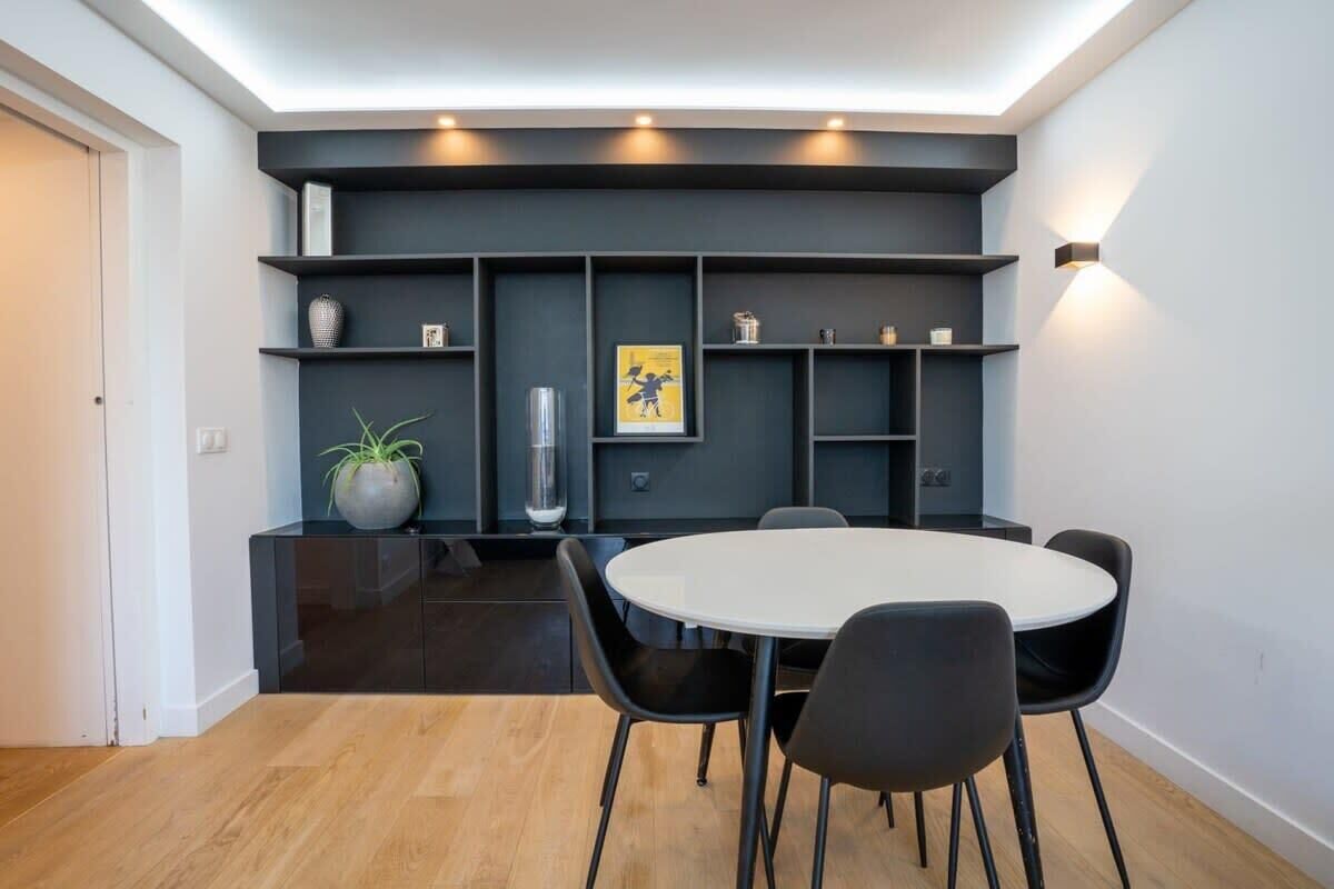 Ein stilvoller Essbereich mit einem runden Tisch und schwarzen Stühlen, einer dunklen Wand mit Regalen und einer Topfpflanze.