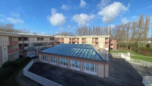 Un edificio de varios pisos con un área central cubierta por techo de vidrio, rodeado de balcones y una terraza de madera.