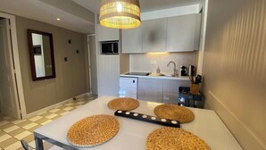 Cocina moderna con microondas, lavamanos y armarios blancos. Hay una mesa de comedor con individuales tejidos y una lámpara colgante.