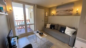 Sala de estar con sofá, una mesita y un televisor. Hay una puerta corrediza de vidrio que da a un área exterior con barandilla.