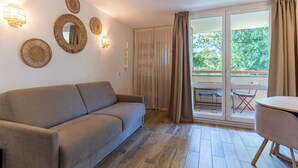 A room with a sofa, a table, and a balcony with chairs. - Appt pour 4 pers avec piscine couverte tennis et parking gratuit 227 (Le Touquet-Paris-Plage)