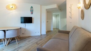 A modern living room with a flat-screen TV, a wooden dining table with chairs, a beige sofa, and a wooden floor. - Appt pour 4 pers avec piscine couverte tennis et parking gratuit 227 (Le Touquet-Paris-Plage)