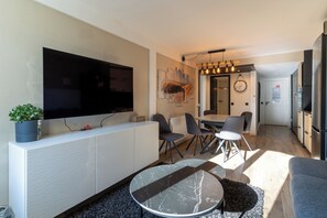 Uma sala de estar moderna com televisão de tela plana, área de jantar com cadeiras e cozinha com geladeira.