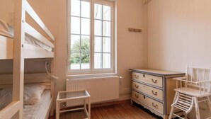 Une chambre d’enfant avec des lits superposés, une commode, une chaise et une fenêtre donnant sur un paysage verdoyant.