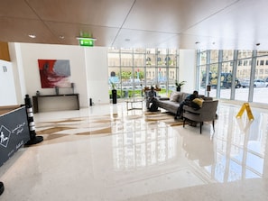 Um lobby moderno com balcão de recepção, área de estar e grandes janelas com vista para a rua.