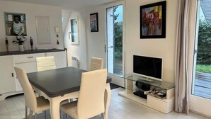 Une cuisine moderne avec un coin repas, un téléviseur posé sur un meuble en verre et des œuvres d’art accrochées aux murs.