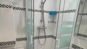 Une salle de bain moderne avec une douche à parois de verre, des toilettes blanches et un lavabo avec un miroir.