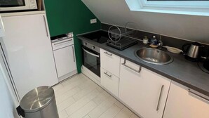 Une cuisine compacte dotée d’un puits de lumière, de meubles blancs, d’un évier en acier inoxydable et d’une poubelle.