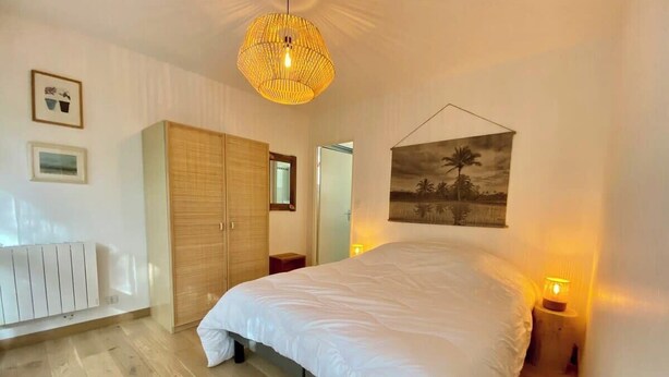 A bedroom with a large bed, a wooden wardrobe, a radiator, and a wall-mounted picture.