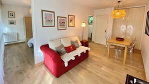 A living room with a red sofa, a dining table with chairs, and a pendant light.
