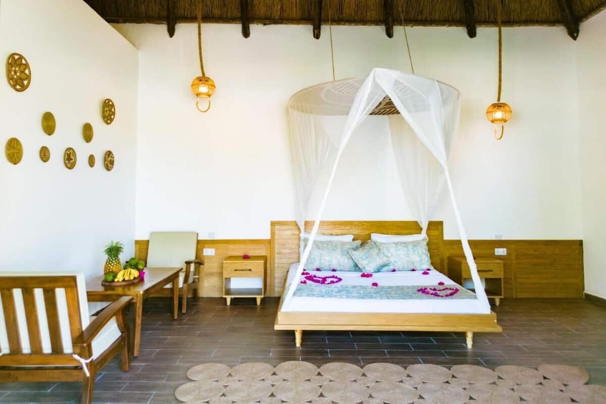 A bedroom with a bed under a canopy, wooden furniture, a small table with fruits, and wall decorations.