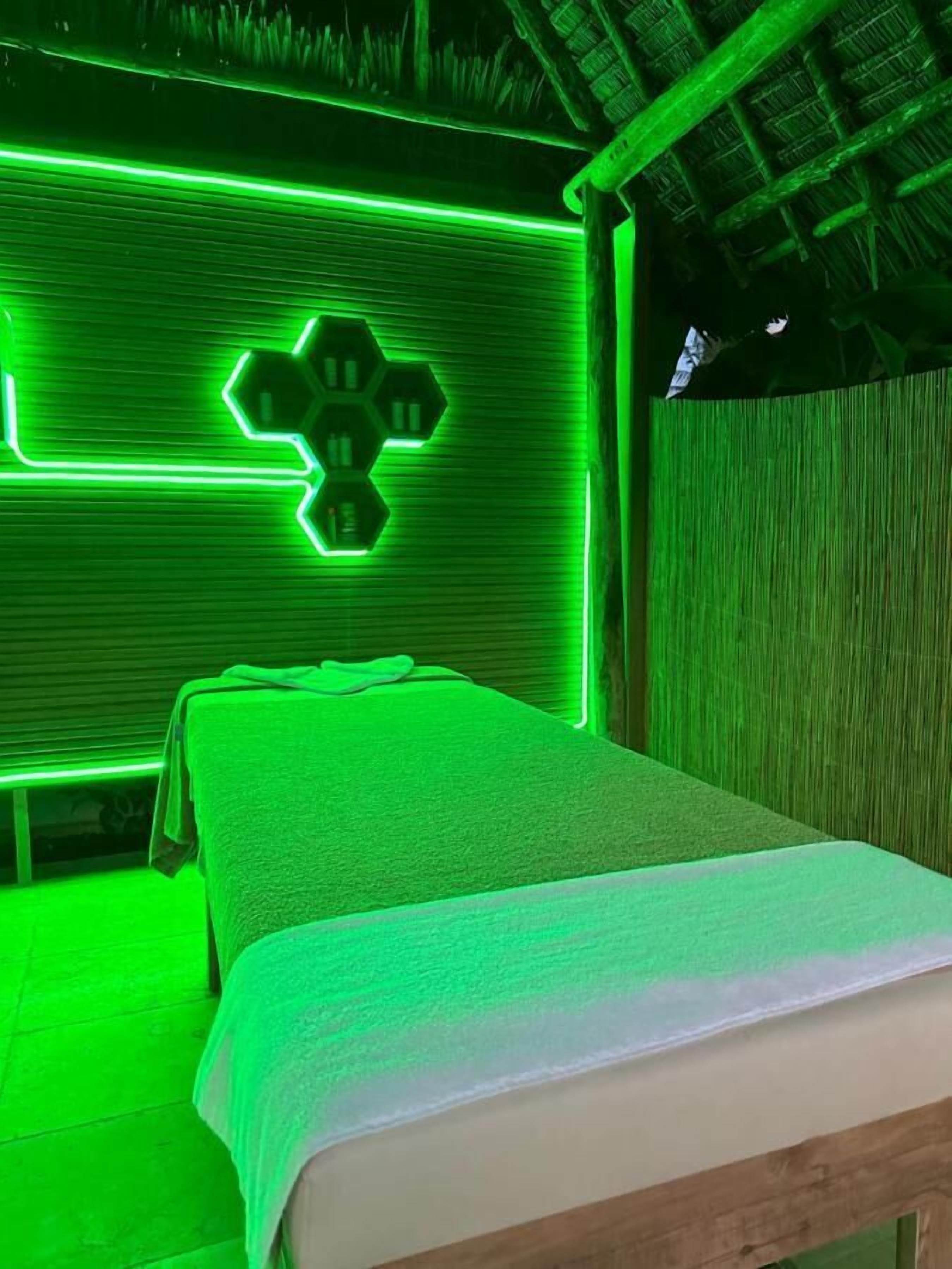 A room with a bed, a green neon light design on the wall, and a wooden ceiling.