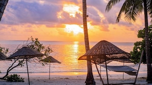 A beach scene with palm trees, beach umbrellas, and a sunset over the ocean. - Turkuaz Beach Hotel (Kiwengwa)