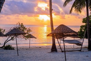 Di pantai, pasir putih, kursi berjemur, dan payung pantai
