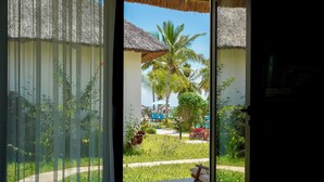 A view from a room with a glass door to a tropical garden with palm trees and a pathway. - Turkuaz Beach Hotel (Kiwengwa)