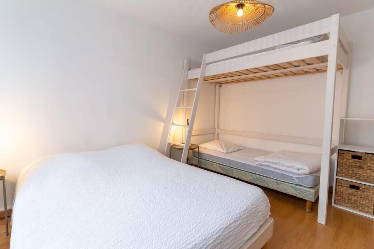 A bunk bed with a ladder, a bedside table, and a hanging light fixture.