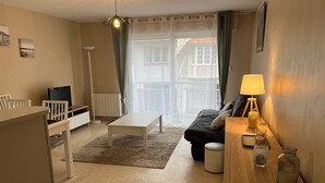 A cozy living room with a white coffee table, a sofa, a TV, and a lamp on a wooden side table.