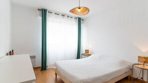 A bedroom with a bed, a bedside table, a lamp, a window with curtains, and a ceiling light.
