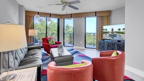 A modern living room with a grey sofa, red chairs, a coffee table, and a television on a stand. - Award-Winning Resort Amenities | Shipwatch 223D (Isle of Palms)