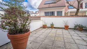 Ein Innenhof mit einer großen Topfpflanze, gefliestem Boden und einem Gebäude mit geneigtem Dach und Fenstern.