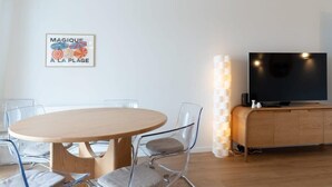 Ein modernes Wohnzimmer mit einem runden Holztisch, transparenten Glaskufen, einem Flachbildfernseher auf einem Holzschrank und einer wandmontierten Leuchte.