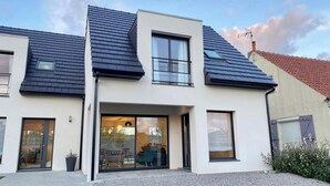 A modern two-story house with a flat roof, large windows, and a sliding glass door leading to an outdoor seating area. - Superb cottage for 4 people with views of the dunes (Merlimont)
