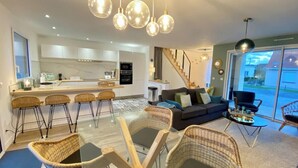 A modern living room with a glass dining table, wicker chairs, a sofa with cushions, and a staircase leading to an upper floor. - Superb cottage for 4 people with views of the dunes (Merlimont)