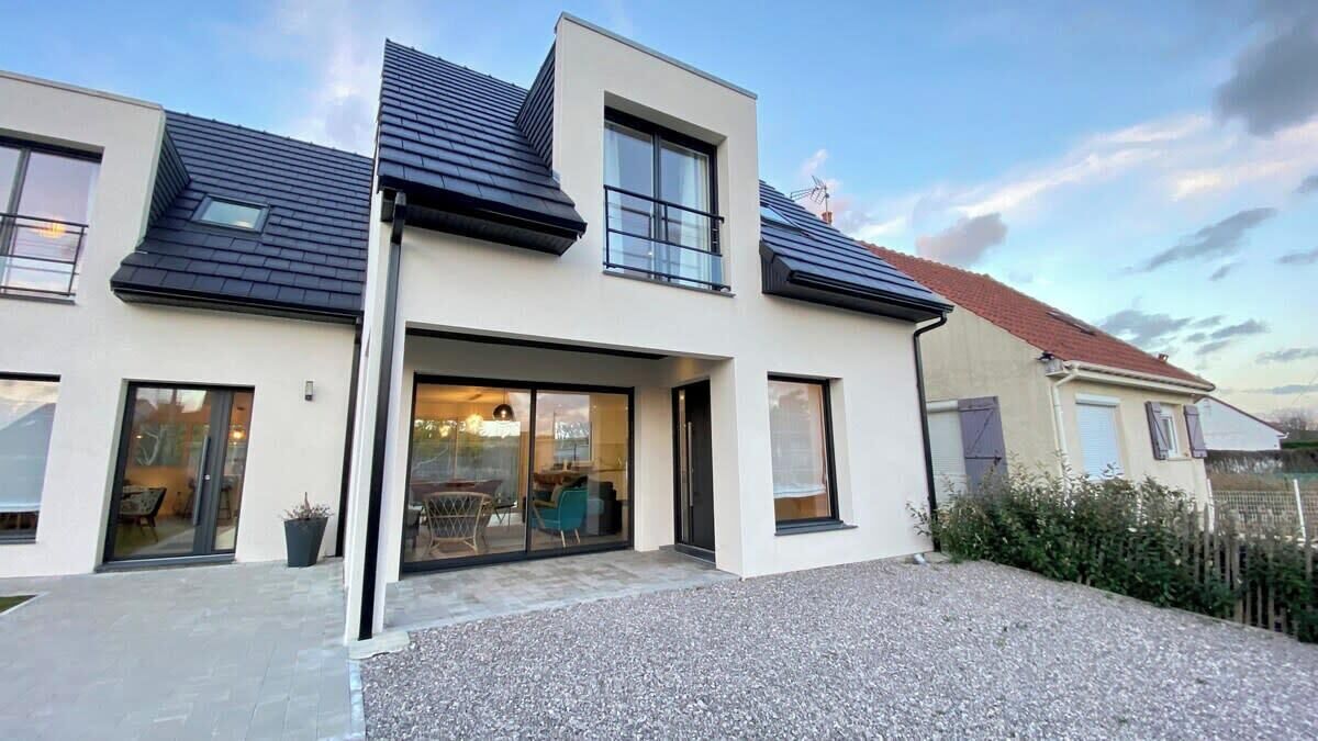 A modern two-story house with a large glass door entrance, a gravel driveway, and a small garden area.