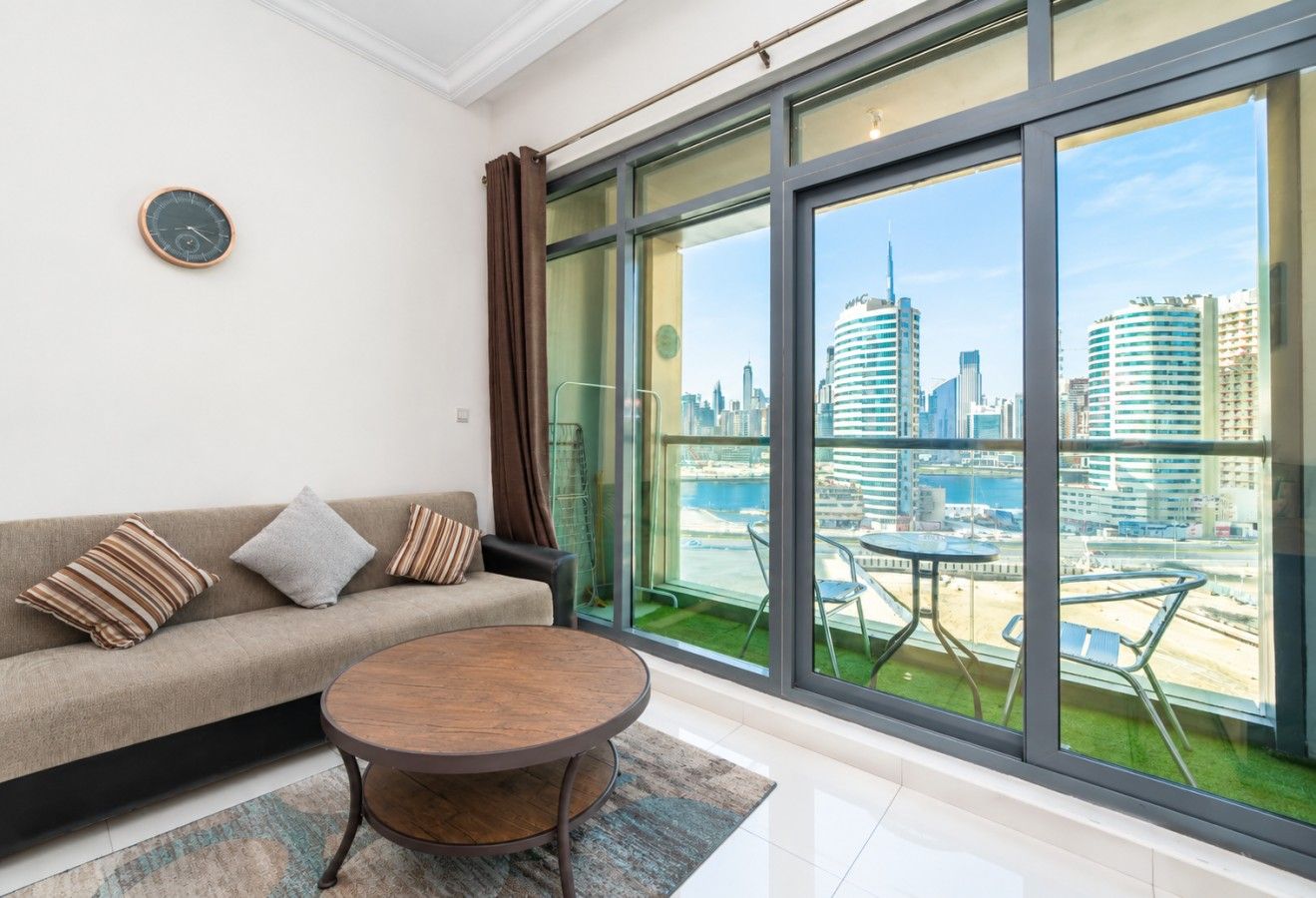 A modern living room with a sofa, a round coffee table, and a large window offering a city view.