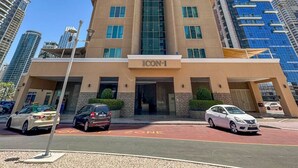A multi-story hotel with a prominent 'ICON-1' sign, a parking area with marked spaces, and a clear sky. - StoneTree - Icon 1 Studio - Cozy Apartment (Jumeirah Lake Towers)