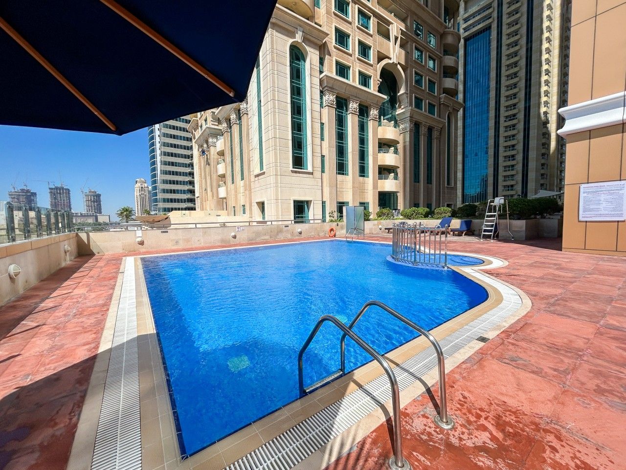 A rooftop swimming pool with a clear view of the city skyline, surrounded by high-rise buildings.