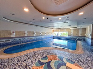 Une piscine intérieure avec un sol et des murs carrelés, entourée d’une plage de piscine bordée d’une rambarde.