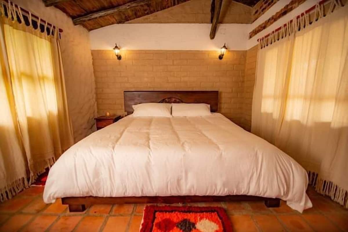 A bedroom with a large bed, wooden headboard, two bedside lamps, and a brick wall.