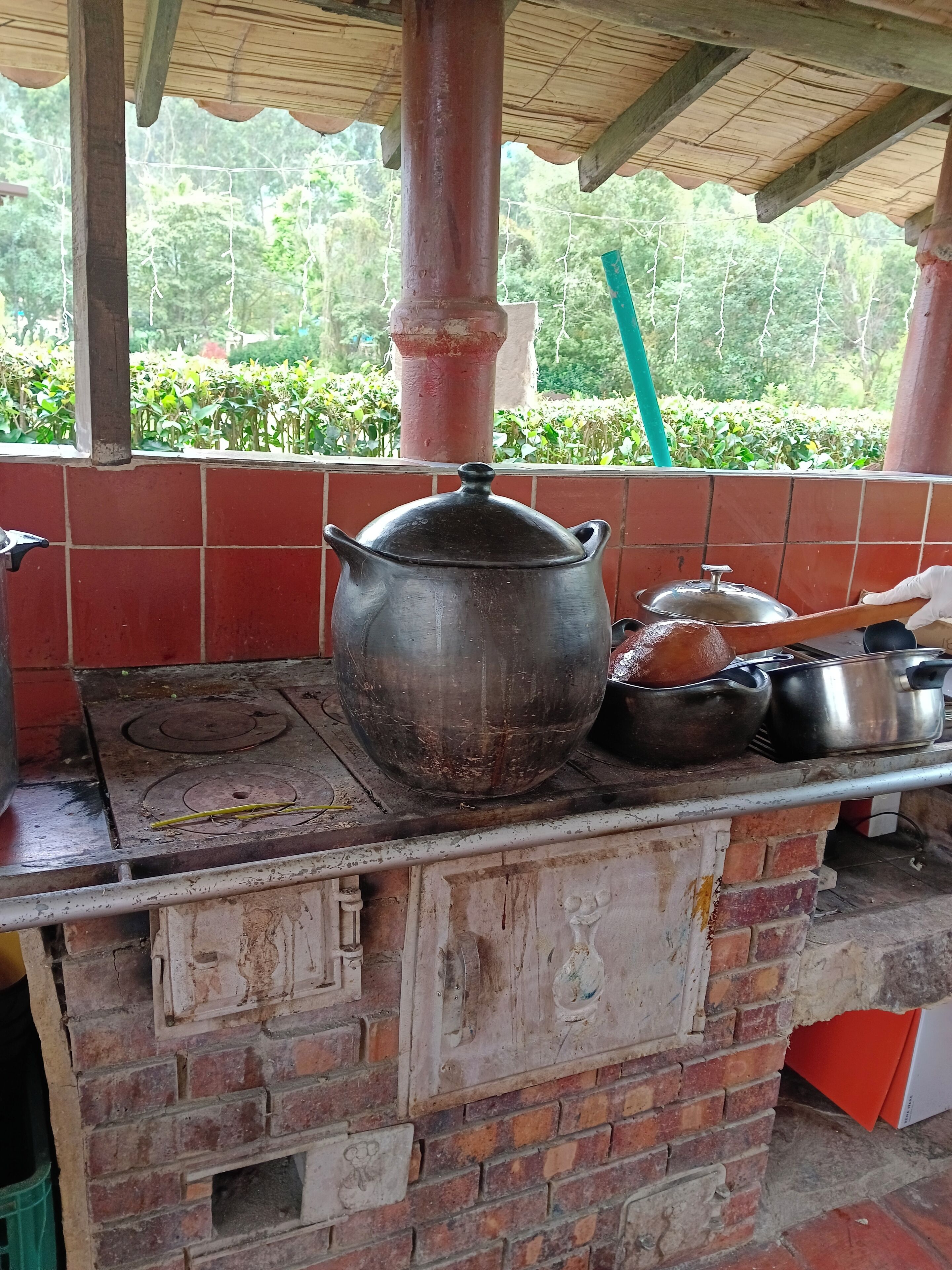 A rustic kitchen with a brick stove, a large pot, and various cooking utensils.